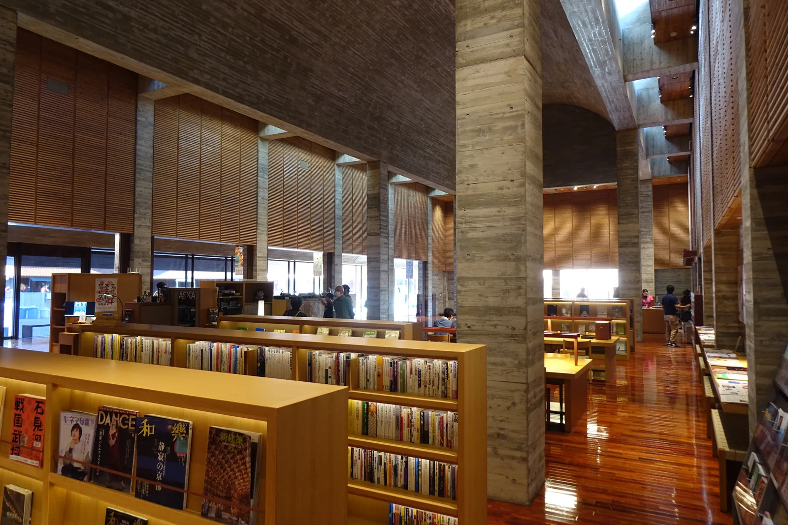 大廳中的 art library，前景是淺色木製的書架與雜誌架，中景是一根粗大的混凝土柱，背景是橫向木板的牆面與明亮的開口
