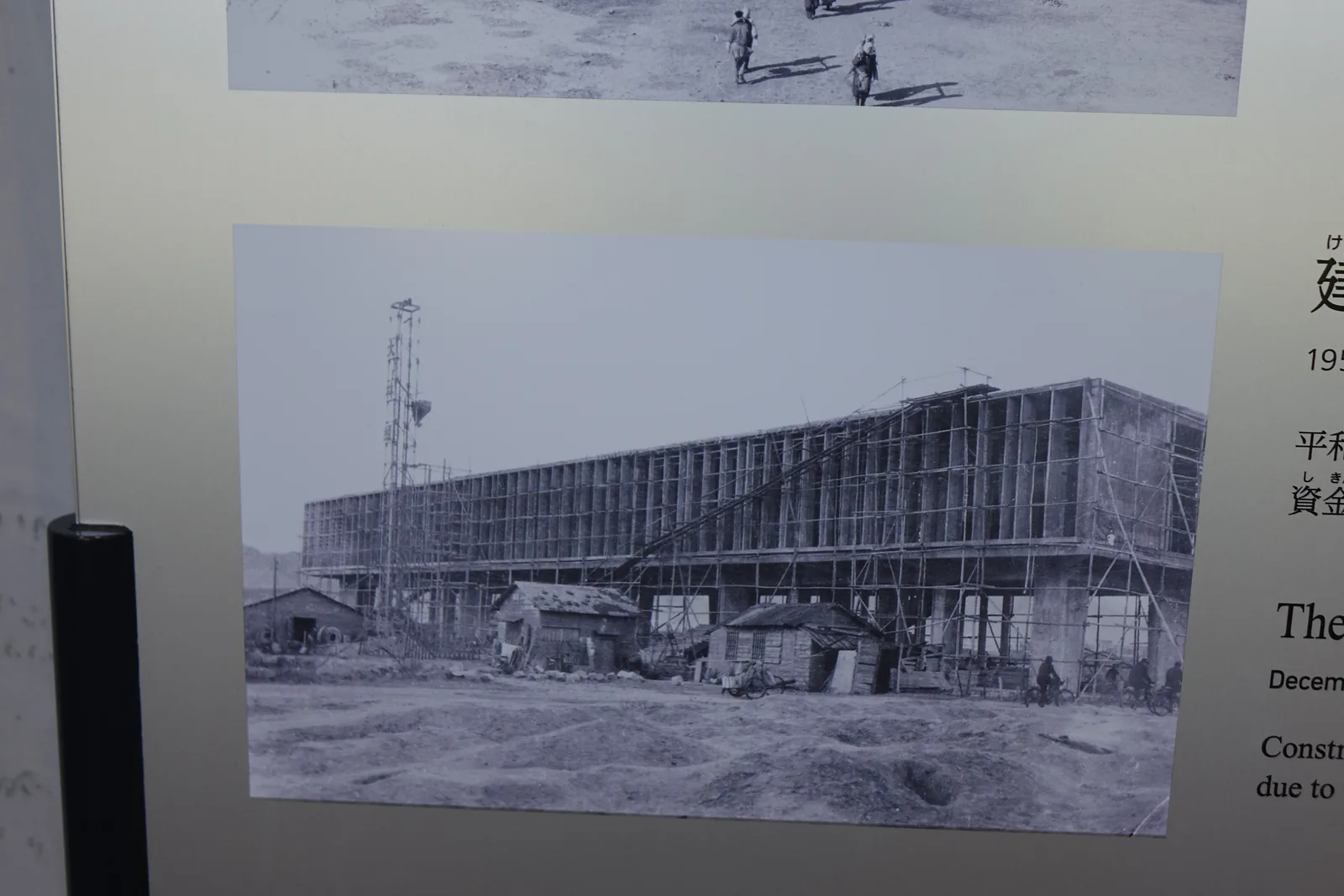 館內展示的一張黑白照片，畫面中是一座施工中的長方形建築，柱與梁的框架已經立起，四周是空地與木造房屋
