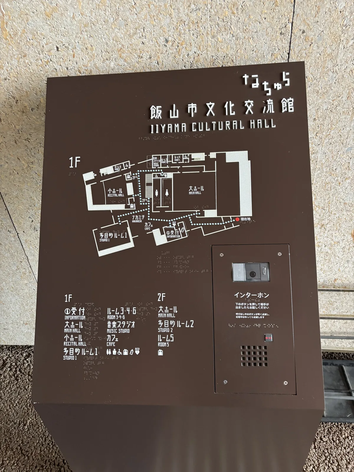 館內的樓層指引，深褐色的金屬面板上以白色線條繪出一樓與二樓的平面，上方印有館名與英文名稱，右側有對講機