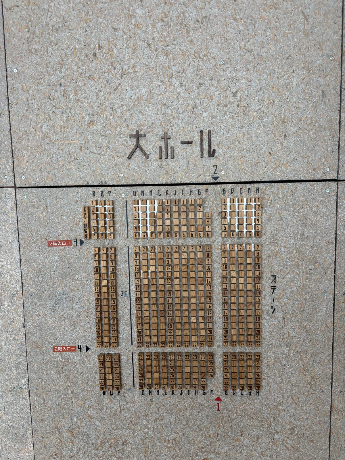 石材般的灰色牆面上，鑲著大表演廳的座位圖，座位以細小的木塊排列成格狀，上方以黑色字標示表演廳名稱，兩側標示入口與舞台