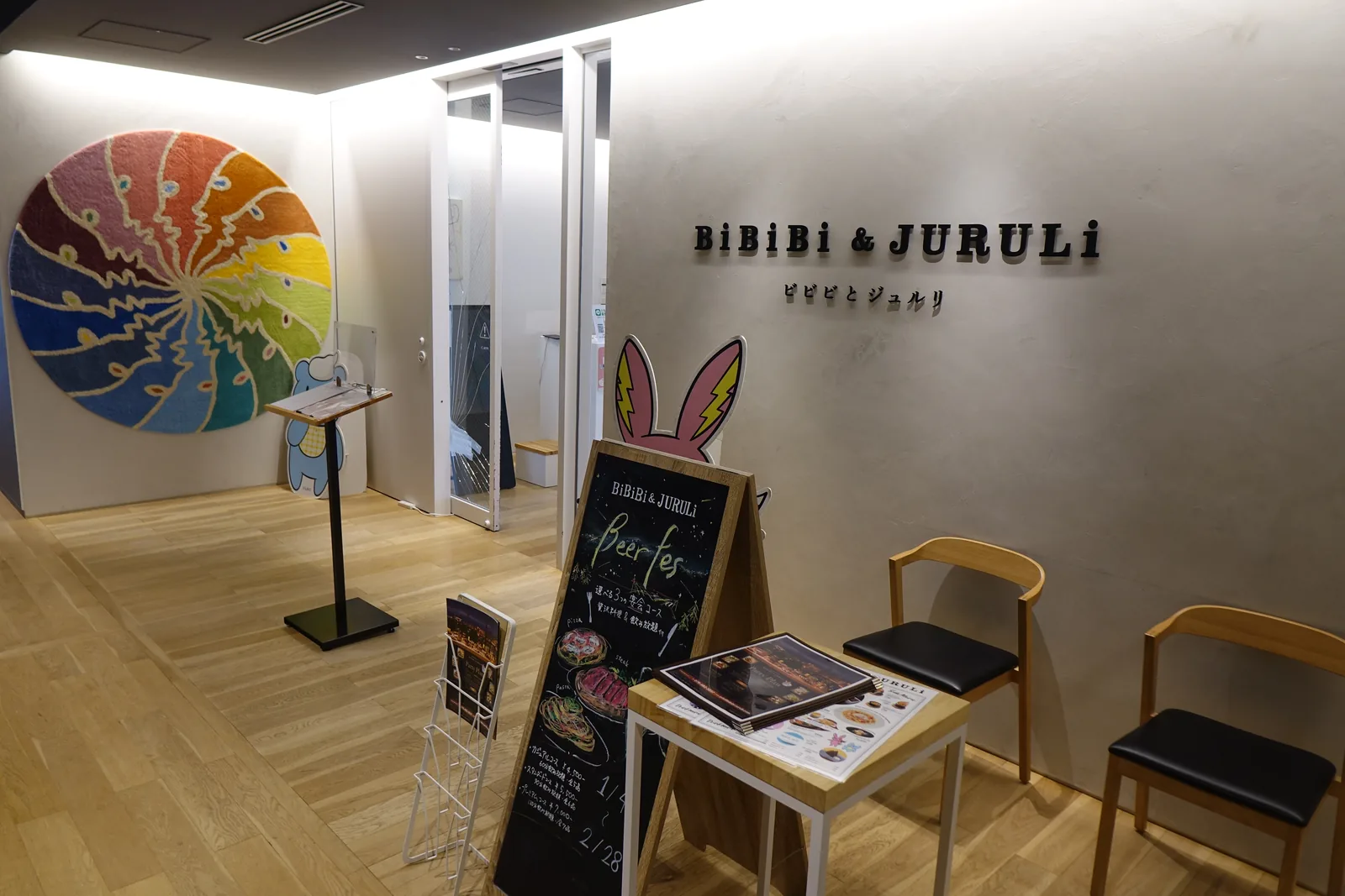 三樓餐廳的入口，左側牆上是一件彩色的圓形色輪作品，右側牆上以黑色字寫著餐廳名稱，入口前放著一塊黑板立牌與幾張木椅，地面是木地板