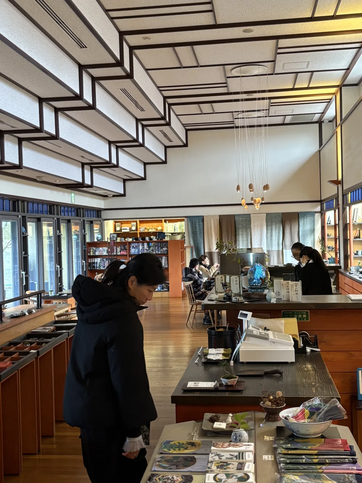二樓的商店，前景是一張放著陶器、書籍與明信片的展示台，右側是一座深色的櫃台與收銀機，左側是一位正在看商品的參觀者，後方是排滿陶器的層架與茶房的座席，天花是格狀的木線條