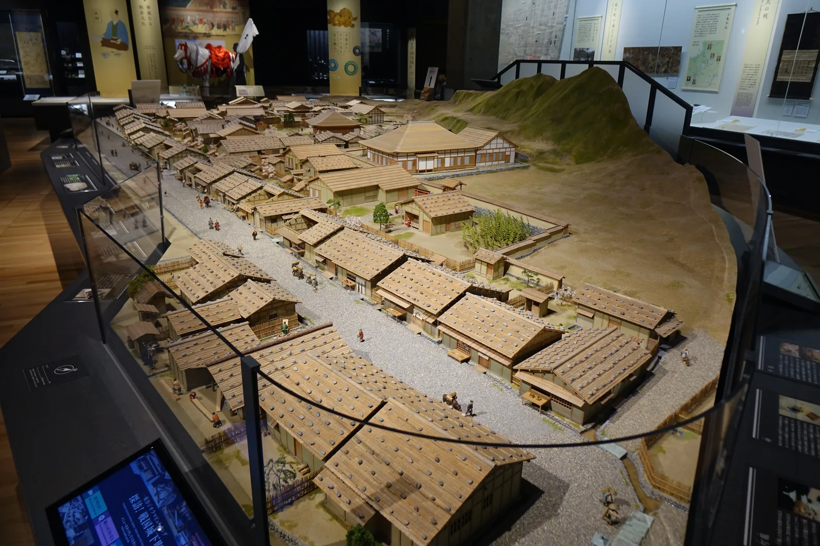 基本展示室中央的城下町模型，一條筆直的道路兩側排著成列的板葺屋頂町屋，屋頂上壓著石塊，遠處是武家屋敷的圍牆與山坡，模型的周圍是玻璃護欄