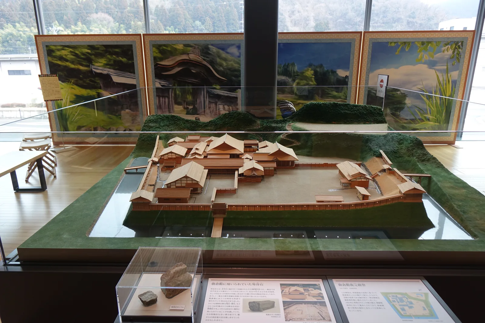 二樓的一間展示室，中央的展示台上是一座朝倉館的木製模型，模型的周圍是綠色的地形，背後的牆上掛著數幅館的復元圖，再後方是一整面玻璃與窗外的山