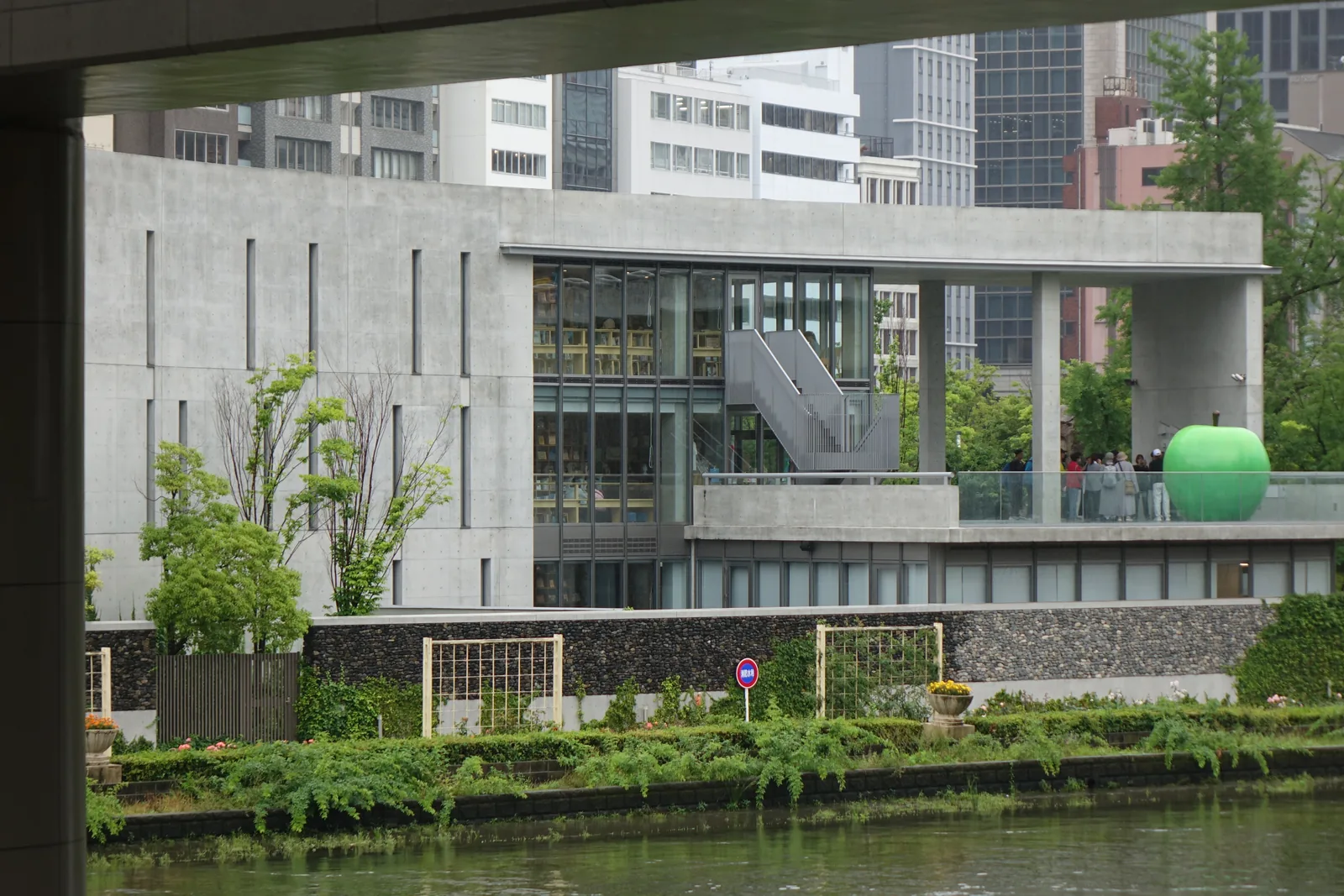 隔著堂島川所見的圖書館北面，一道清水混凝土的長牆上開著數條直向的細縫窗，右段是三層高的玻璃面，可見內部的書架與樓梯，其右是門形構架下的露台與一顆綠色的大蘋果，建築之下是石砌的護岸與河畔的綠地