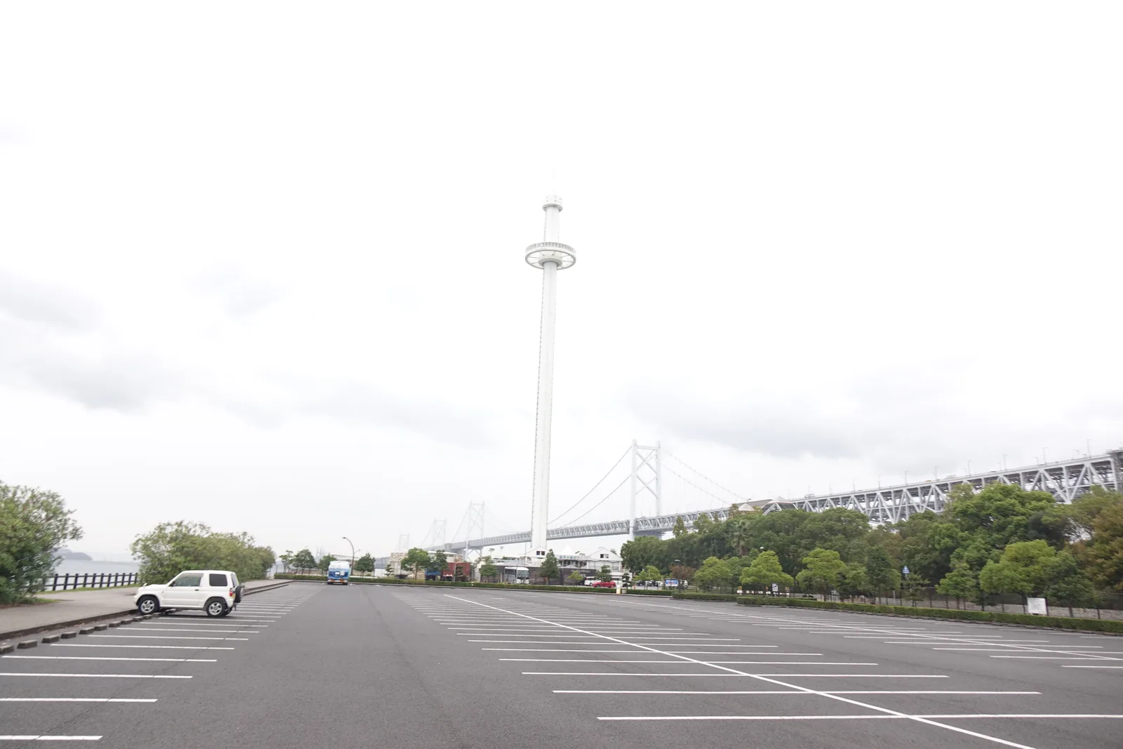 瀨戶大橋紀念公園西停車場，一片空曠的柏油地上畫著白色停車格，遠處是白色的瀨戶大橋塔與向右延伸的瀨戶大橋