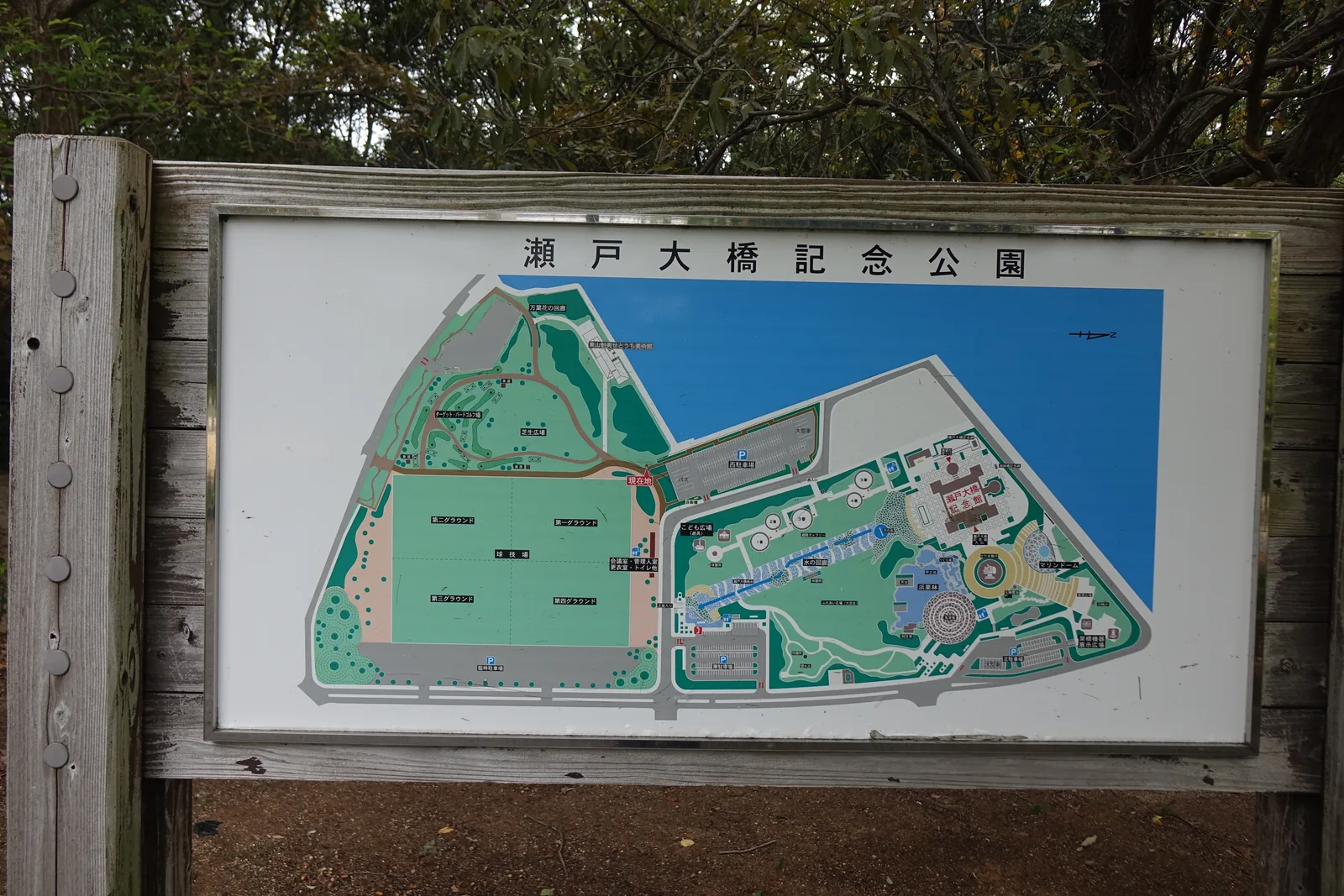 瀨戶大橋紀念公園的園內圖看板，木框中的圖面以綠色表示草坪與樹林、藍色表示海面，標出園內的設施與步道