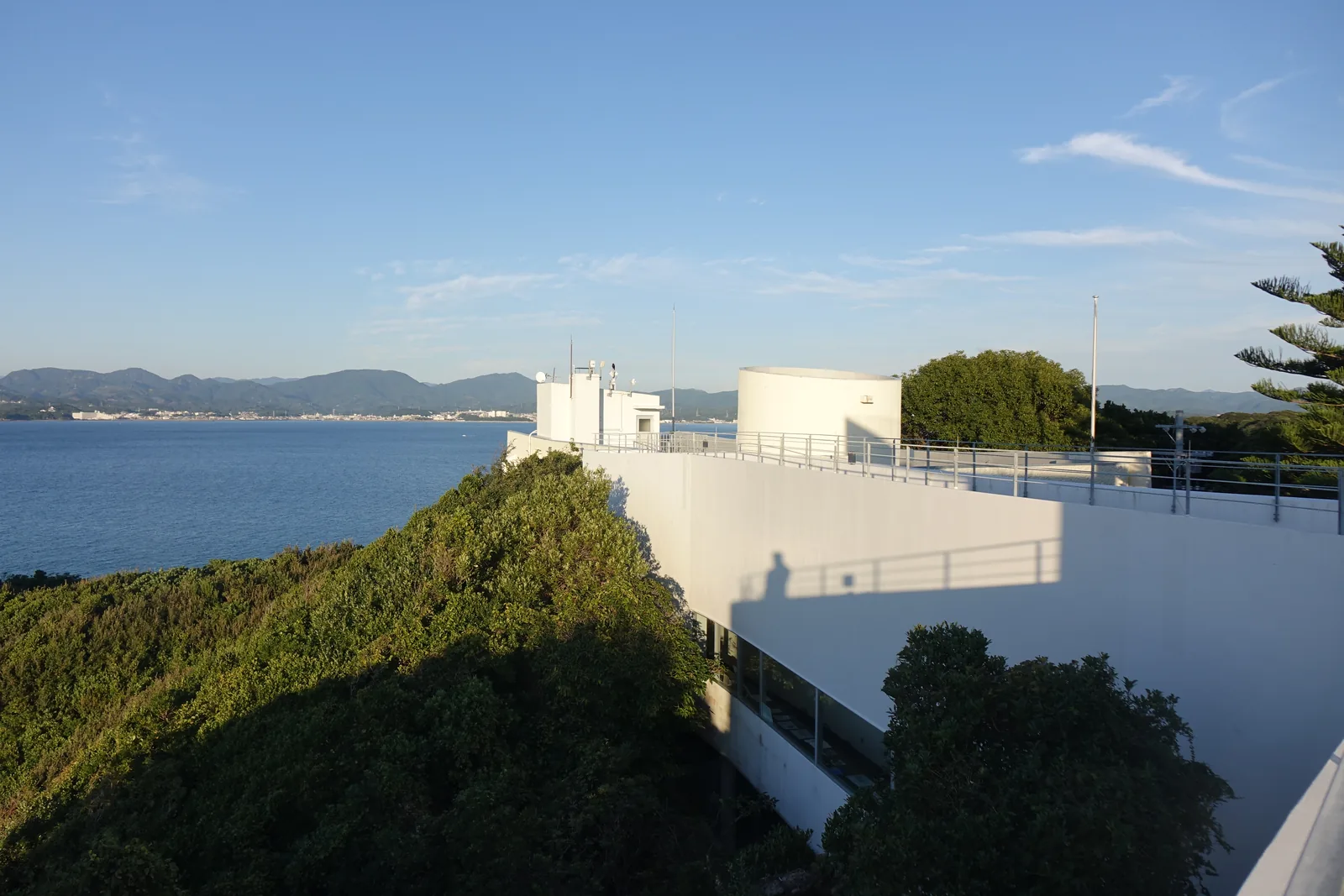 新館屋頂的步道，以白色的牆與欄杆圍出，步道沿著弧線向前延伸，右側是 lantern 頂端露出屋頂的白色圓筒，遠方是海與山