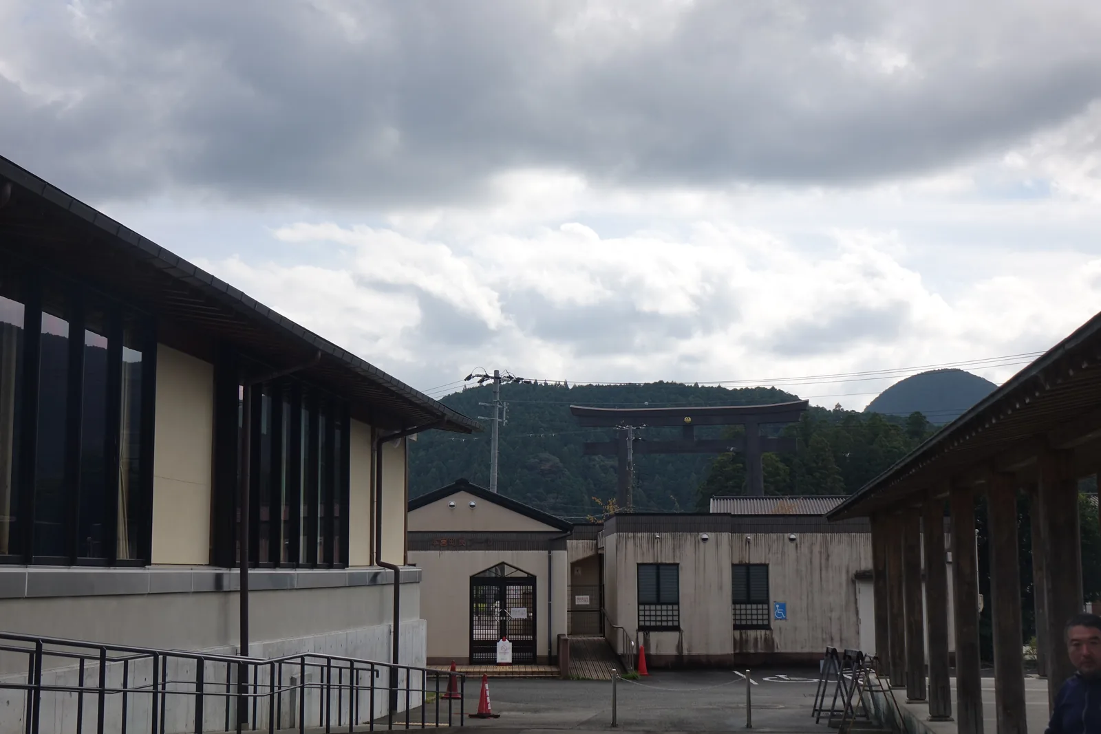 兩棟館舍之間的通道，左右是兩棟館舍的牆面與深出的屋簷，中間是帶有鋼欄杆的坡道與鋪面，盡端是一棟低矮的白牆附屬建築，越過它的屋頂可以看見遠處山腳下的一座巨大鳥居