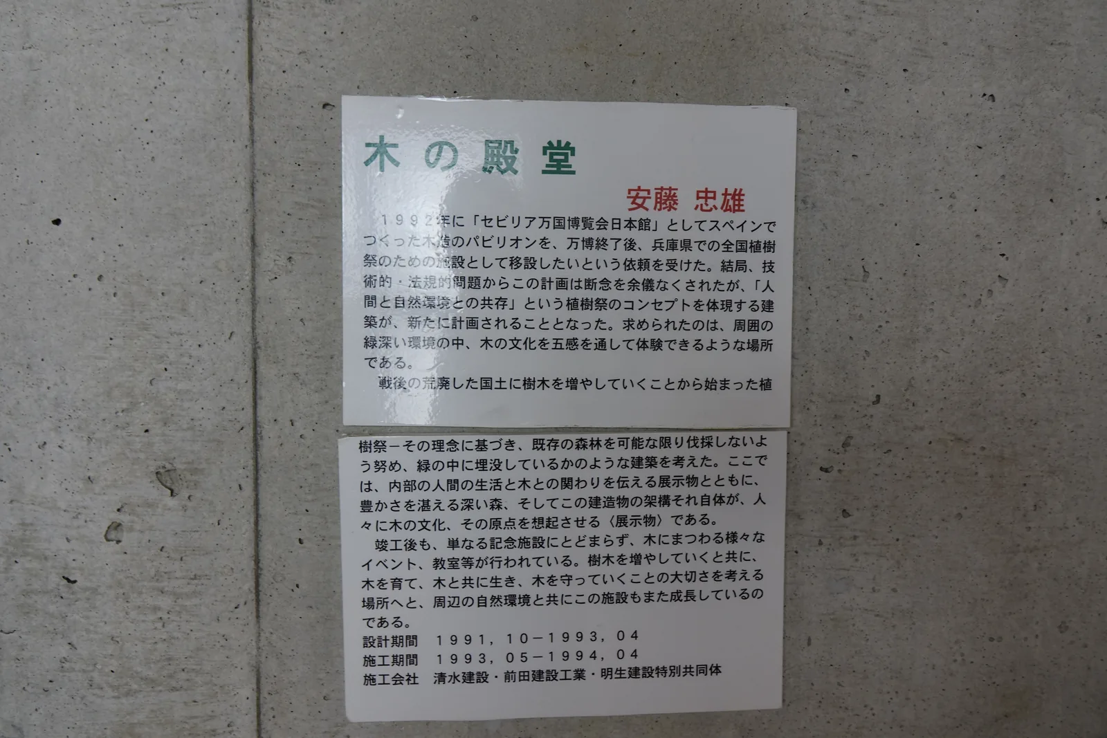 館內清水混凝土牆上的木之殿堂說明牌，標題下署名安藤忠雄，以文字說明塞維亞萬博日本館移設計畫的放棄與新建築的構想，末尾列出設計期間、施工期間與施工公司