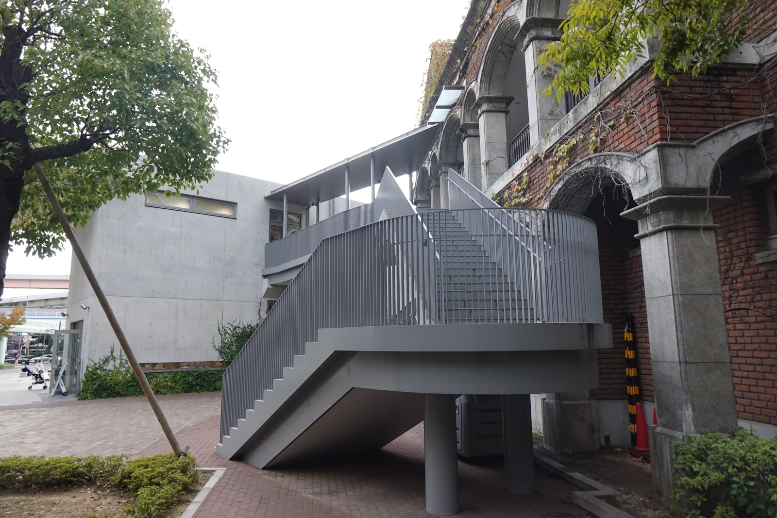 本館與東遊園地管理棟之間的通路，左側是本館的清水混凝土外牆，右側是一棟紅磚拱廊的建築，一座深灰色的鋼製樓梯自地面折返而上，接上連絡兩棟建築的二樓通道