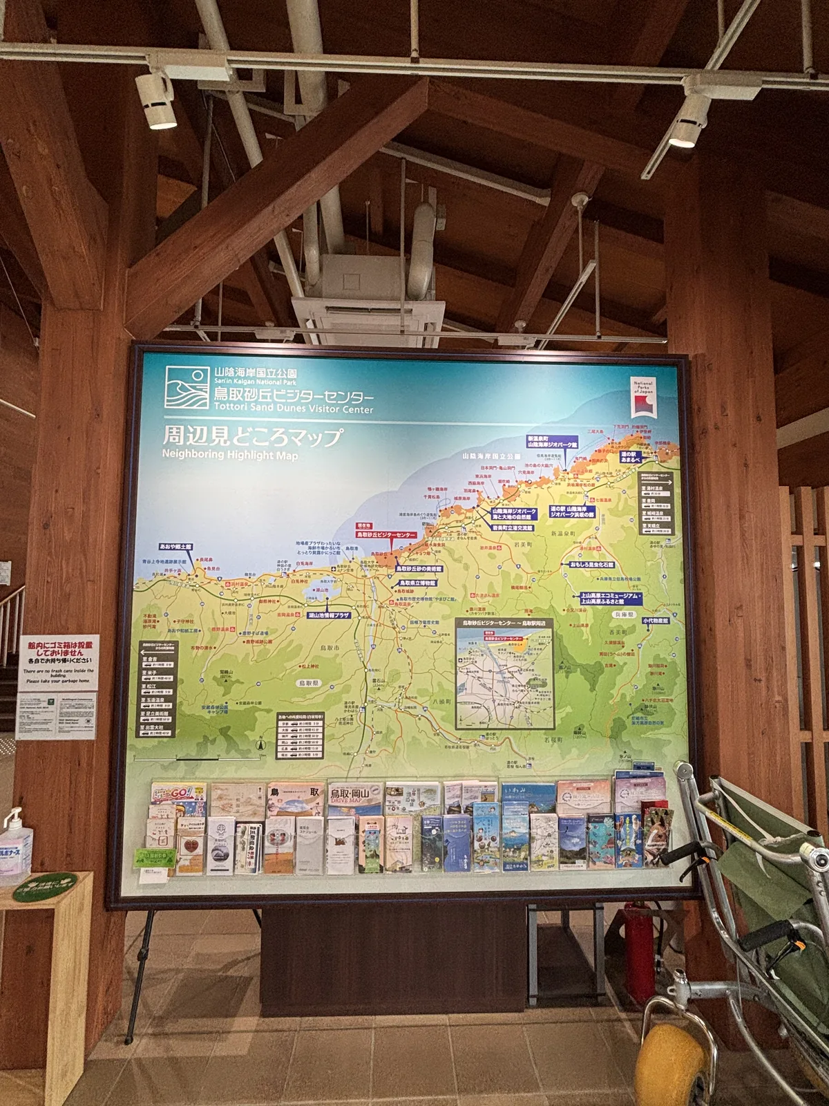 遊客中心入口一帶，前方是一塊大型的周邊觀光地圖看板，看板下方擺放著各種摺頁，上方是木造的柱與斜撐支撐的屋架，天花吊著管線與照明，左側是一根木柱