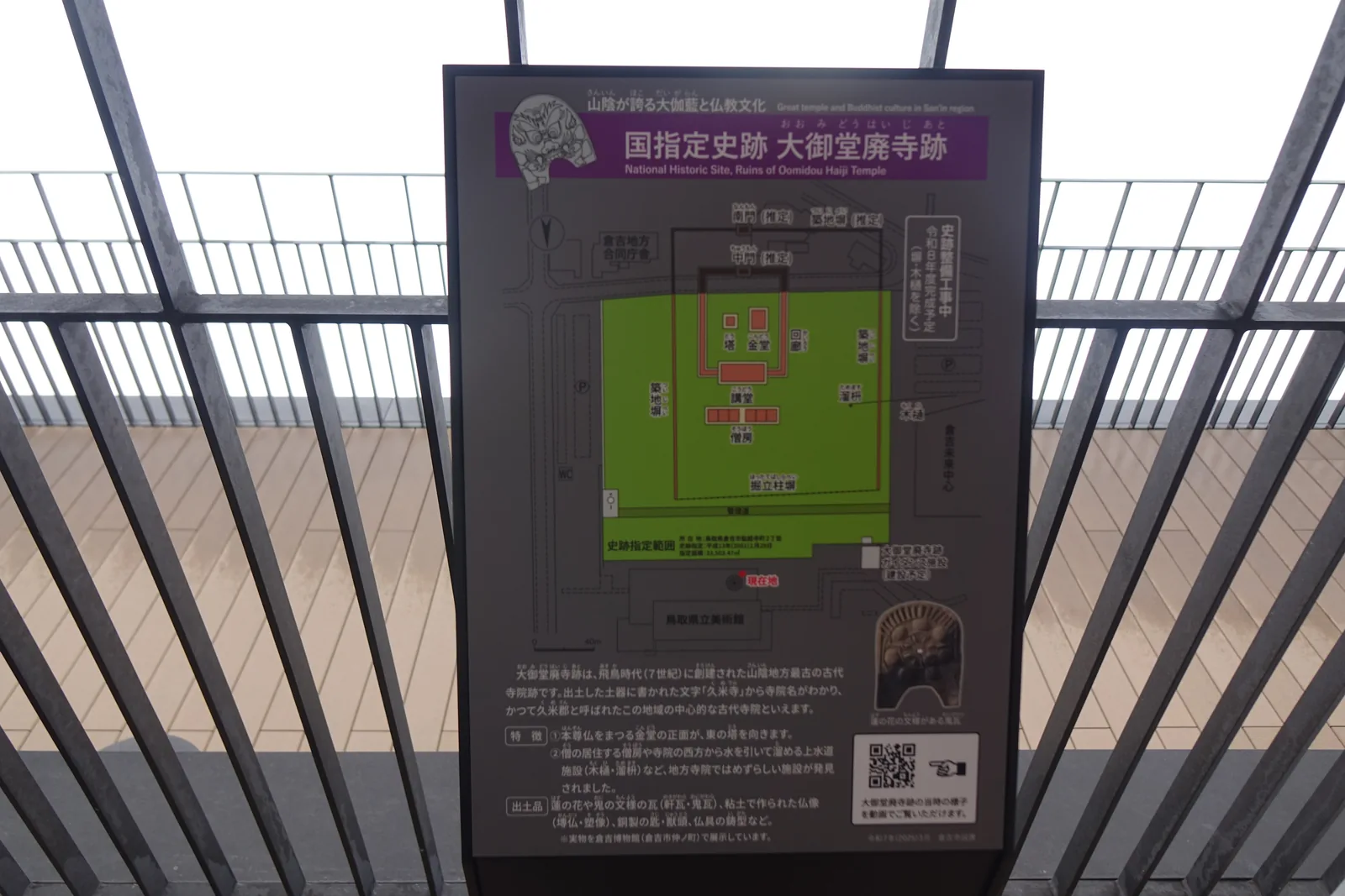 展望露台上的史跡解說板，標題為國指定史跡大御堂廢寺跡，板上是綠色底的伽藍配置圖與說明文字，背後是露台細密的金屬欄杆與天花的木格柵