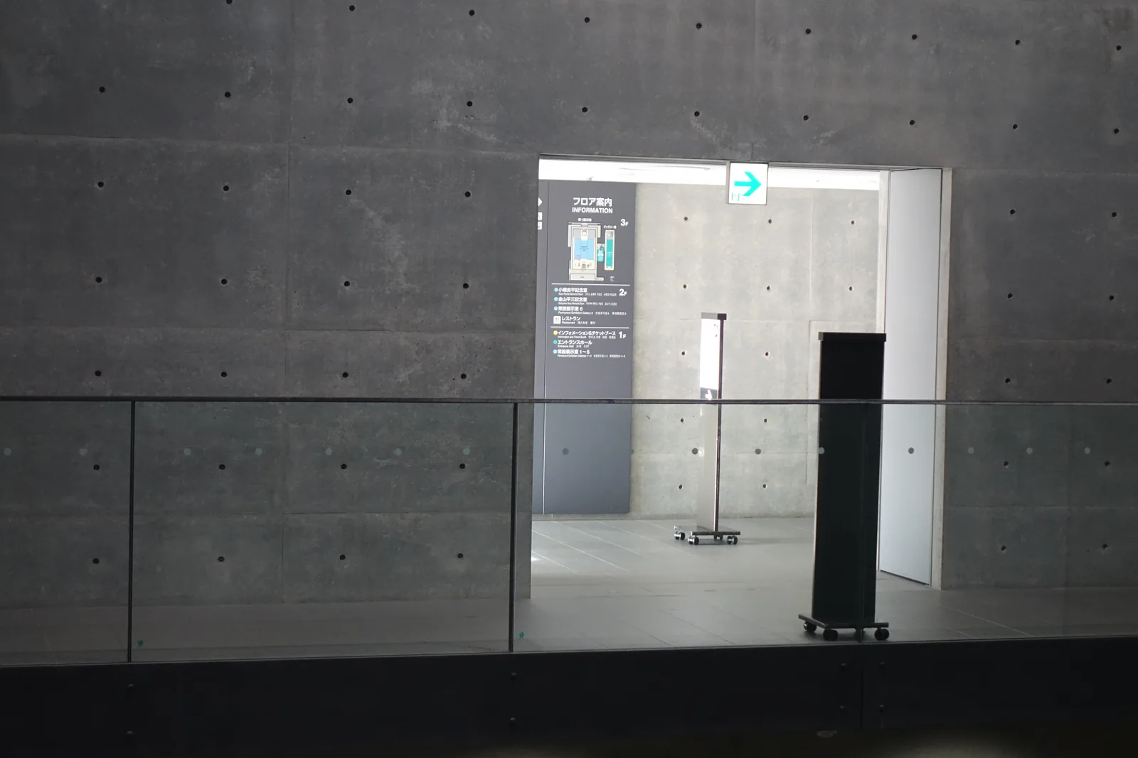 清水混凝土牆上的一個方形開口，開口內是明亮的展示室入口與樓層導覽的看板，開口前是玻璃的欄杆