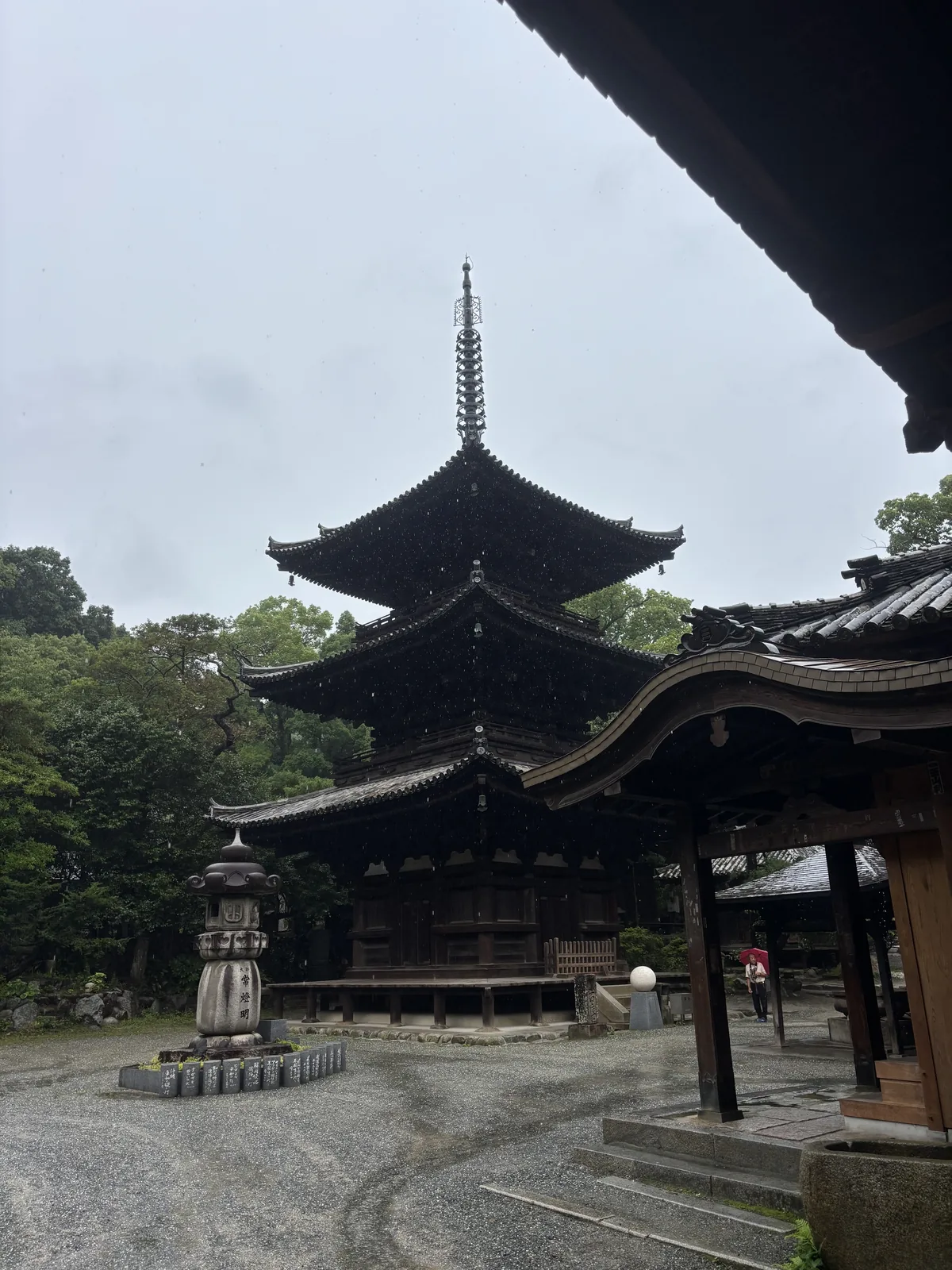 石手寺境內的三重塔，深色木造的三層塔身與出挑的屋簷，前方是石燈籠與鋪石的地面，右上方是另一棟堂宇的屋簷