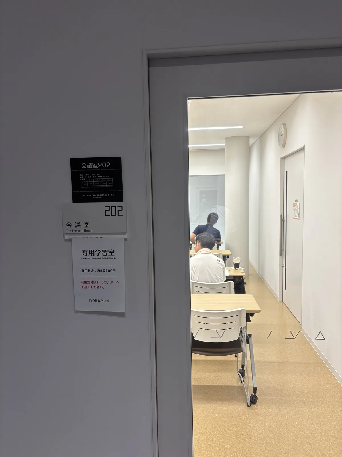 二樓會議室 202 的門口，門邊的牆上貼著會議室名牌與「專用學習室」的告示，門內是一間淺色地坪的長形房間，長桌與椅子沿牆排列，數人背對門口自習，深處是白色的牆與門