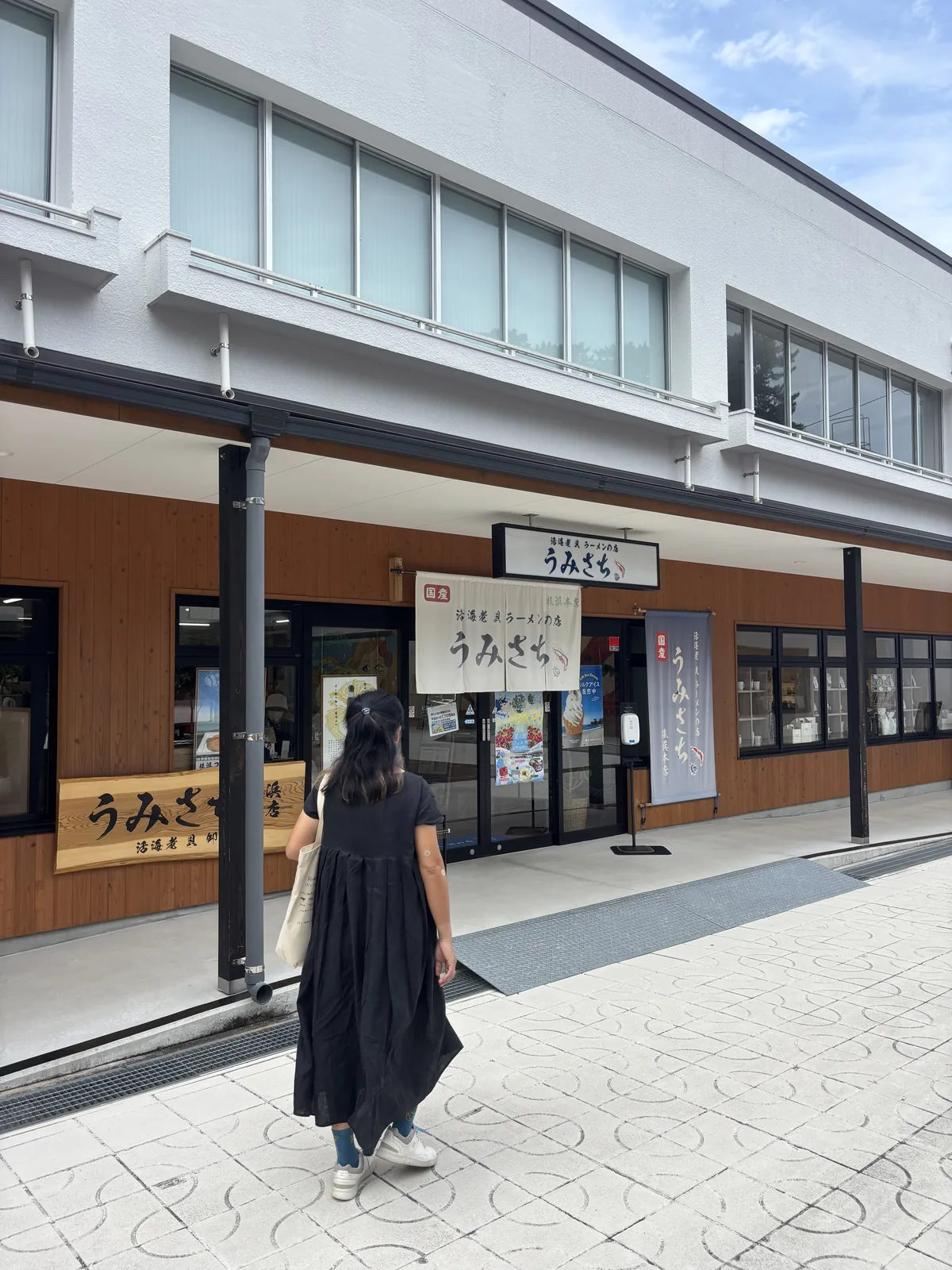 桂浜海之露台的一排店舖，白色的雙層量體下是木紋的店面，懸著寫有店名的白色招牌與暖簾，前方是鋪石的步道