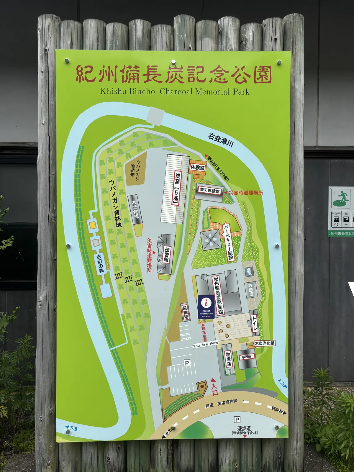 紀州備長炭記念公園的配置圖看板，綠色的公園被藍色的右會津川從北、西兩側環繞，園內標出炭窯五基、體驗窯、加工體驗館、傳習館、木炭倉庫、烤肉設施、紀州備長炭發見館、物產店與事務所，下方是縣道田邊龍神線
