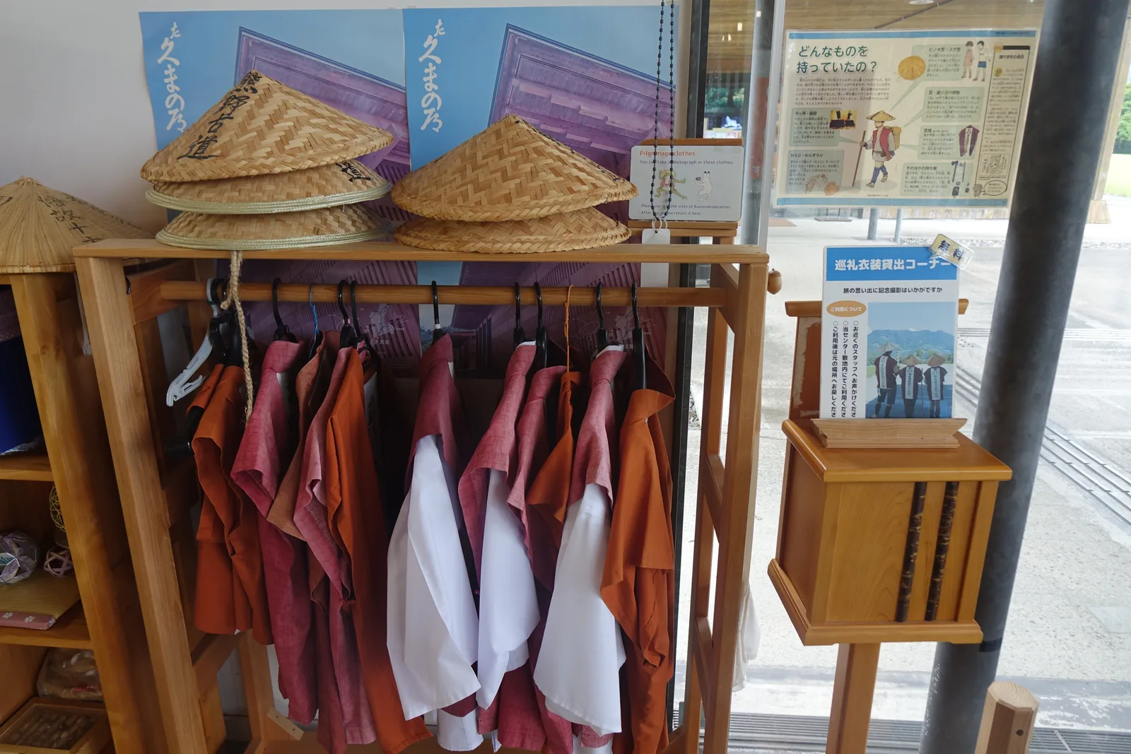 館內靠玻璃面的一角，木製衣架上掛著紅色與白色的巡禮服裝，上方擺著幾頂斗笠，右側是一座木製的說明台與一根鋼柱，玻璃外是館前的鋪面