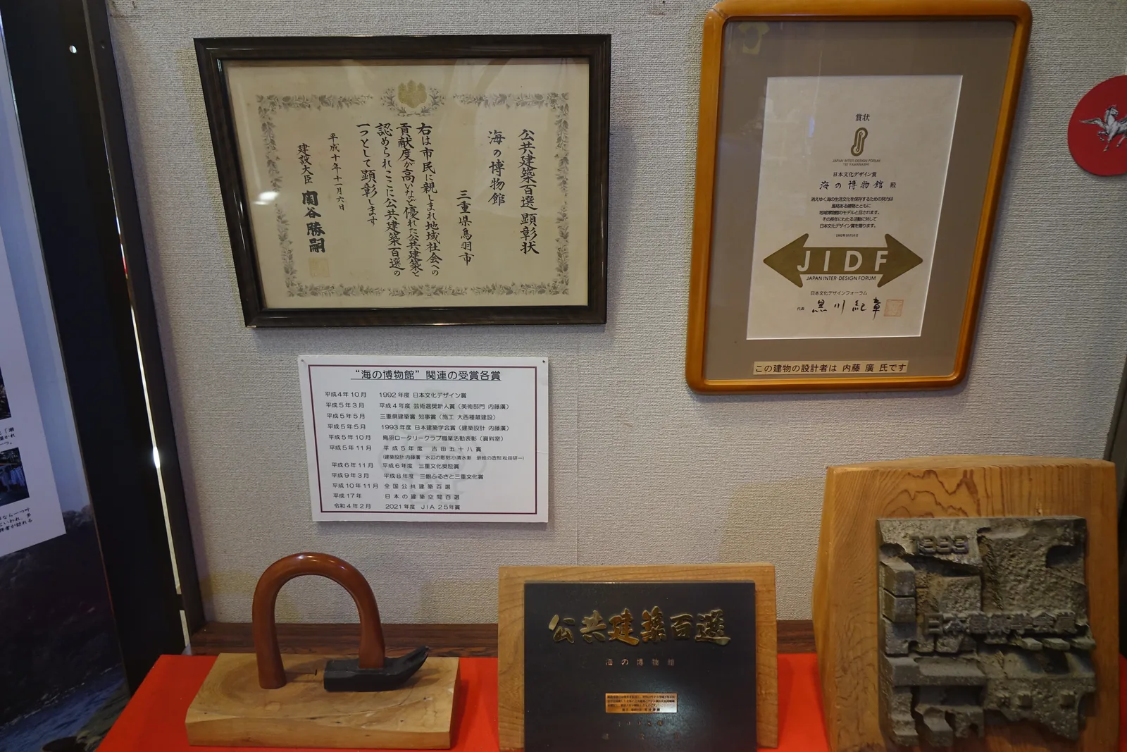 館內陳列的獎狀與獎牌，左側是公共建築百選的表彰狀，右側是日本文化設計賞的獎狀，下方是寫有公共建築百選的牌子、一件金屬工具與一塊壓印紋樣的金屬板