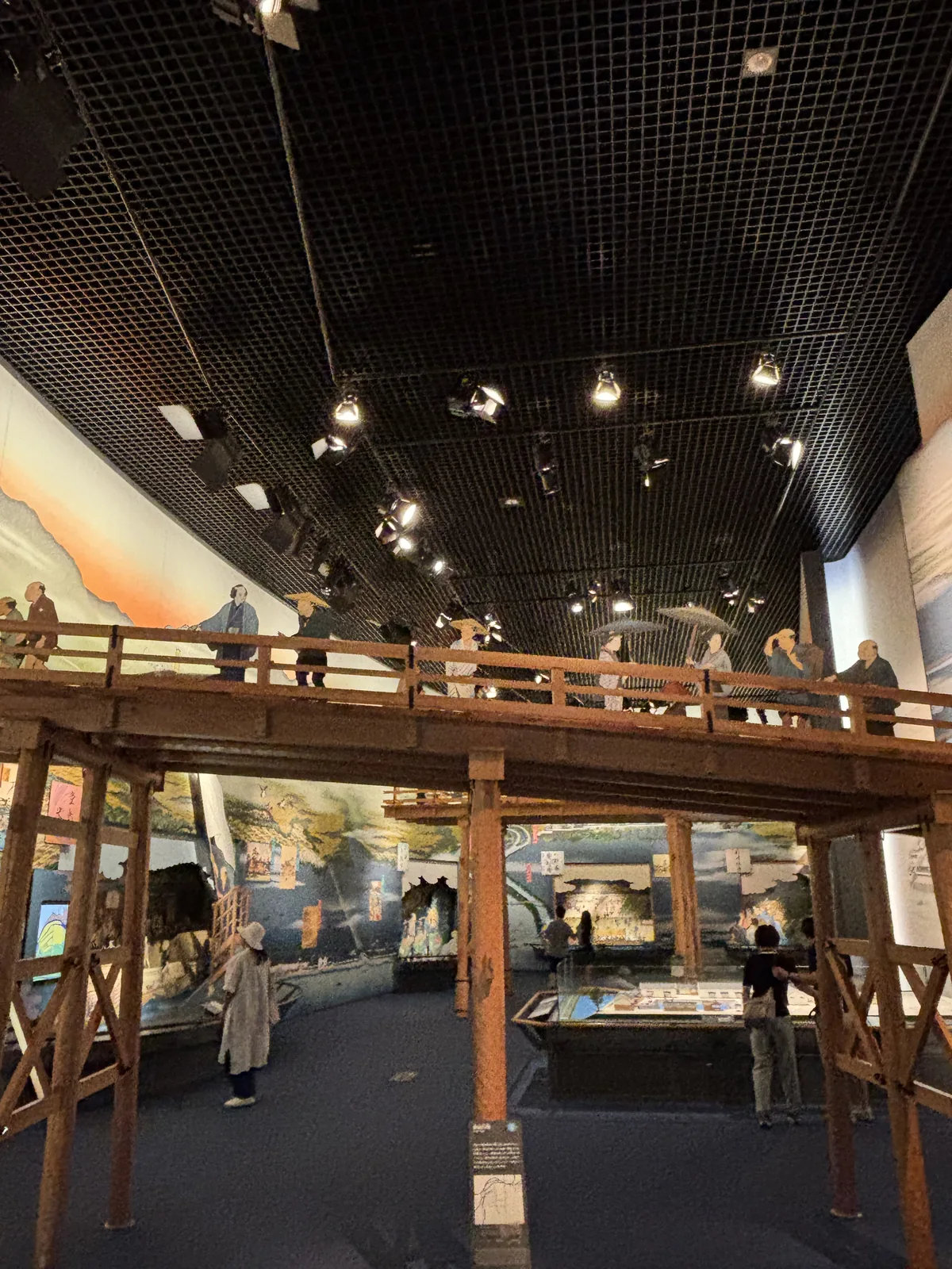 九樓的展示空間，中央是一座木造橋樑的復原，橋上有參觀者，兩側的牆面是描繪大阪河川與港口的大幅壁畫，天花是黑色的格柵與投射燈